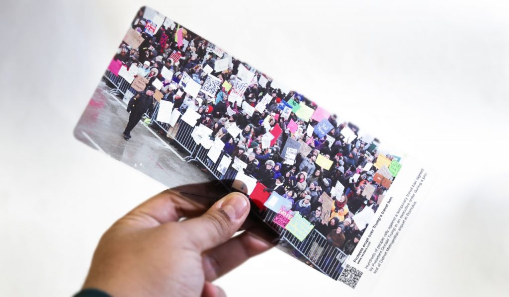 A hand holding a picture of a protest contained behind a fence