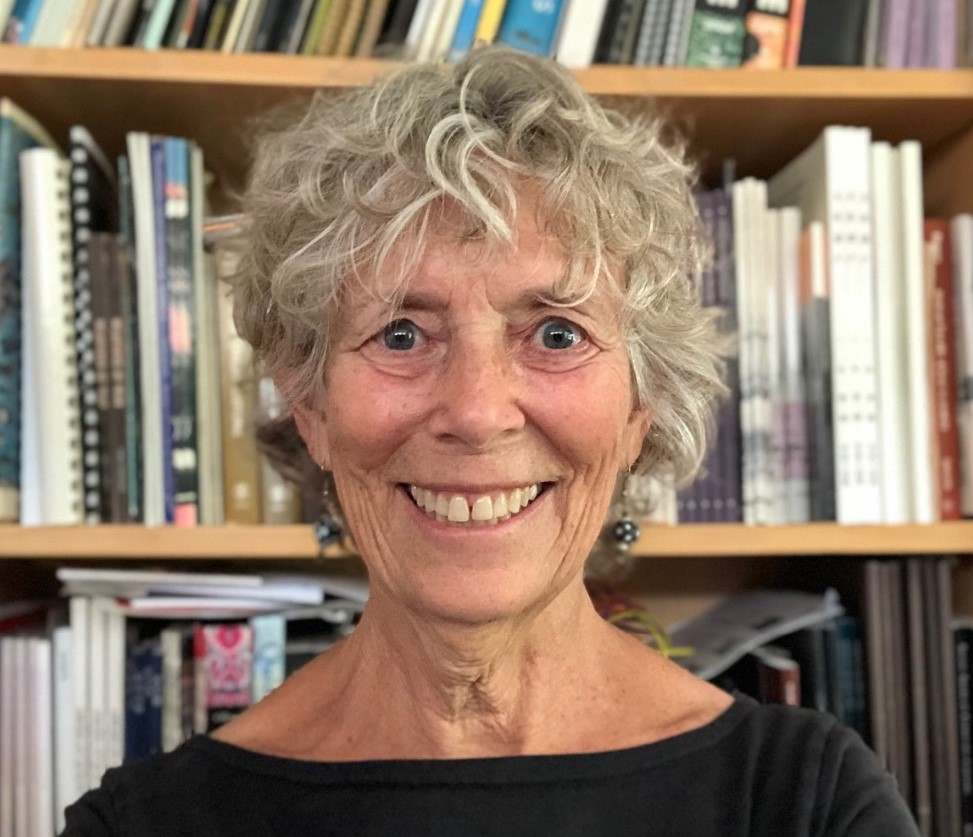 woman wearing a black top with short curly hair smiling at the camera with a bookshelf in the background