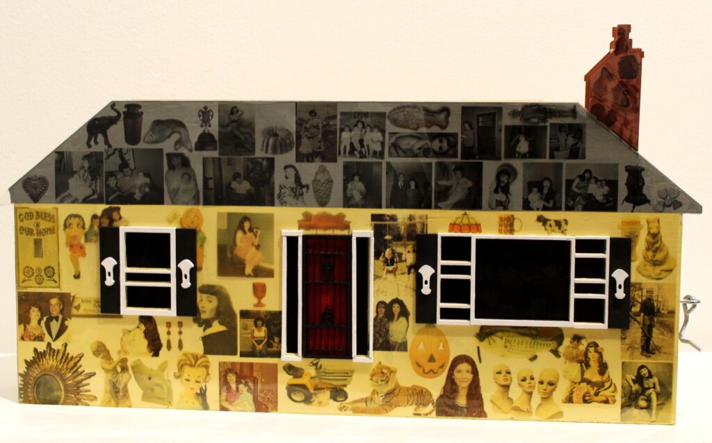 A mixed-media sculpture in the shape of a house, with the façade covered in a collage of vintage photographs, illustrations, and found images