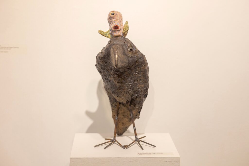 A photo of a clay/ceramic bird figure with a tiny creature sitting on its head.