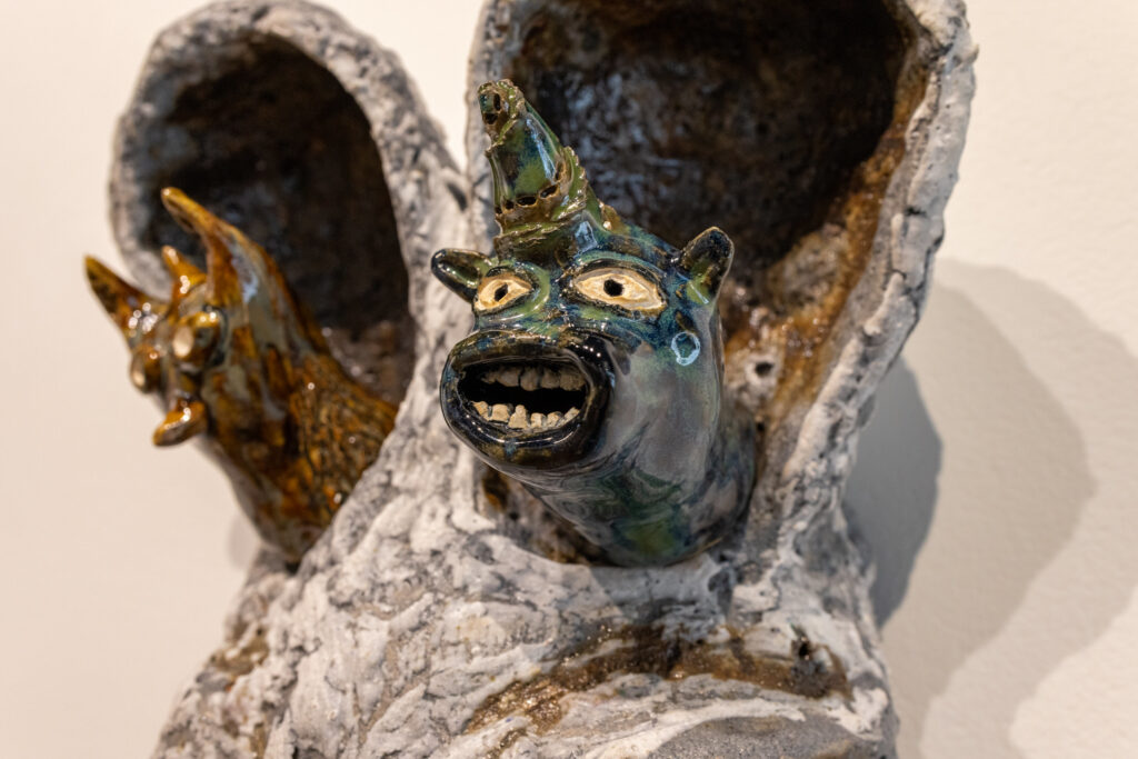 A close up of two ceramic fcafes figures that appear to be poking their faces out of a tree-like sculpture.