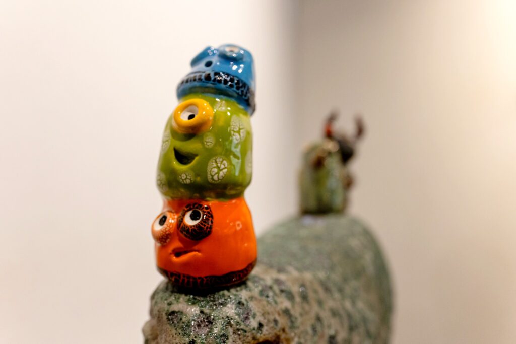A  closeup photo of three brightly colored round weird and silly faces stacked on top of each other, made from clay/ceramic.