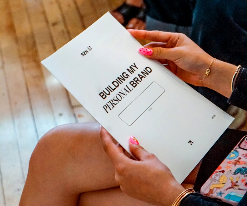 A photo of a person's hands with long nails holding a white pamplet that says "Building My Personal Brand" on the front.