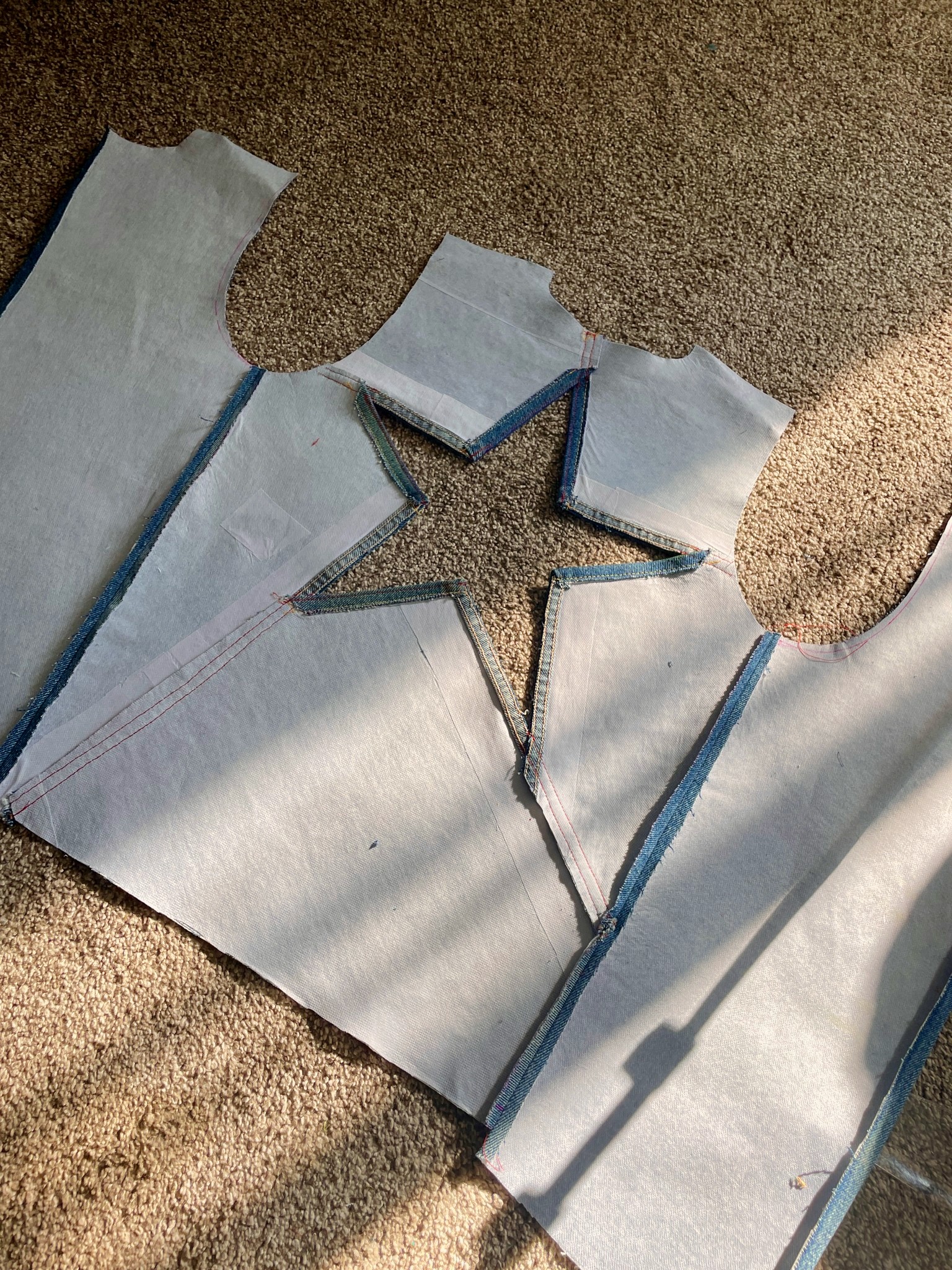 Paper sewing patterns are laid over denim fabric on a carpeted floor. The pattern includes a large star cutout in the center.