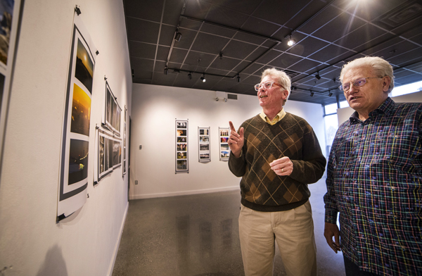 Two men standing next to each other looking at pictures in a photo exhibit
