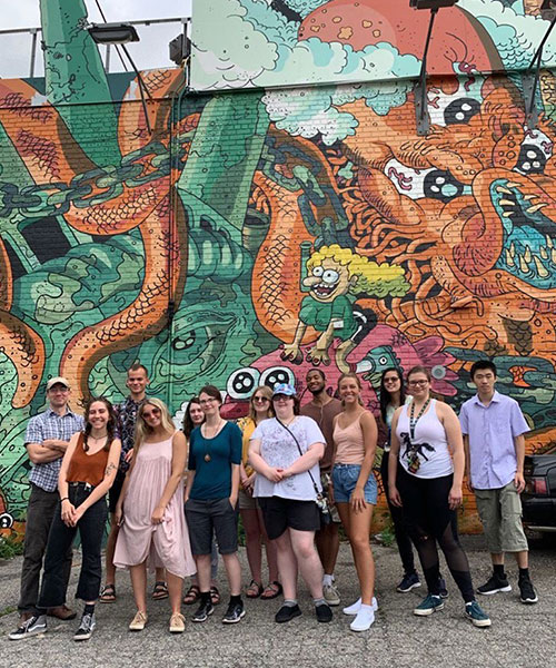 Group of thirteen people in from of a mural with a dragon on it