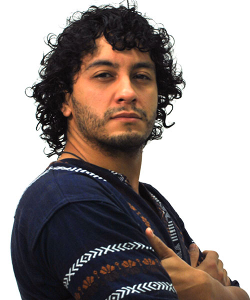 man with curly black hair is standing to the side. He is wearing a navy shirt with white and orange print
