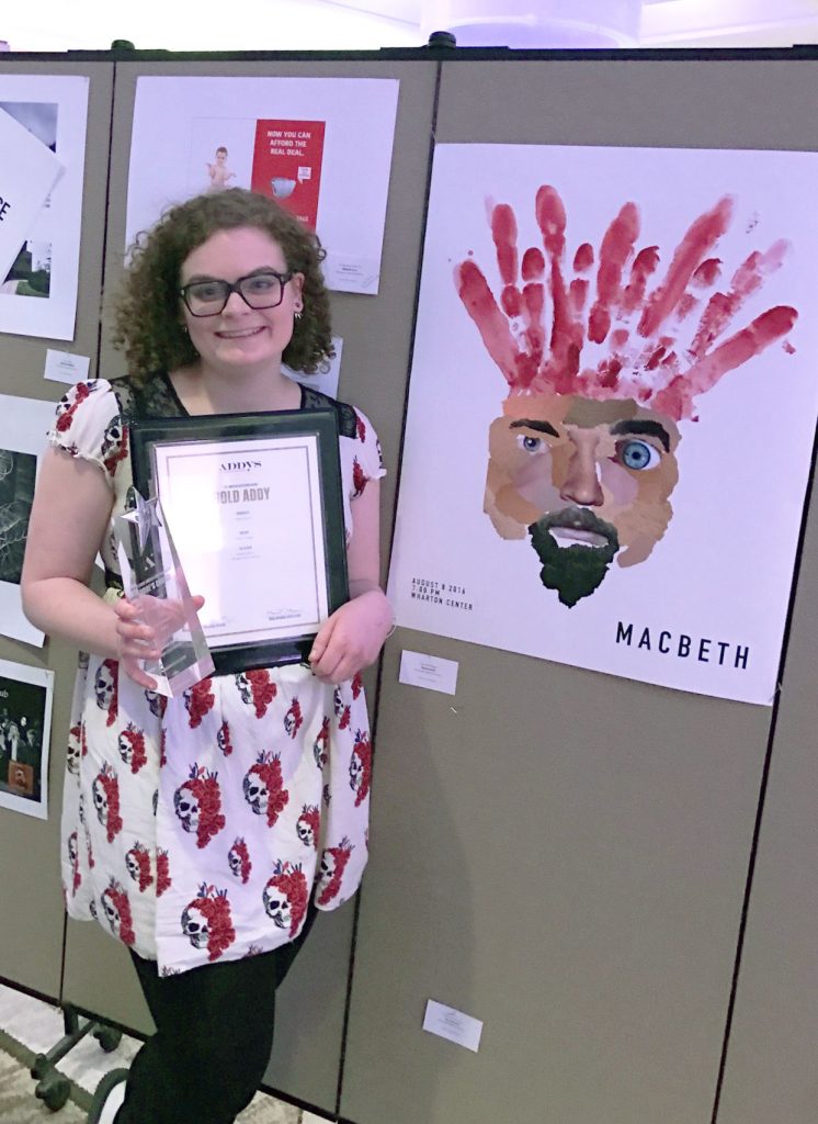 Woman with curly brown hair is holding an award next to her painting