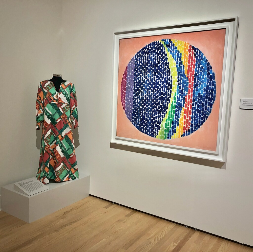 Exhibit of a red, green, and orange dress next to a framed painting of a multicolor circle.