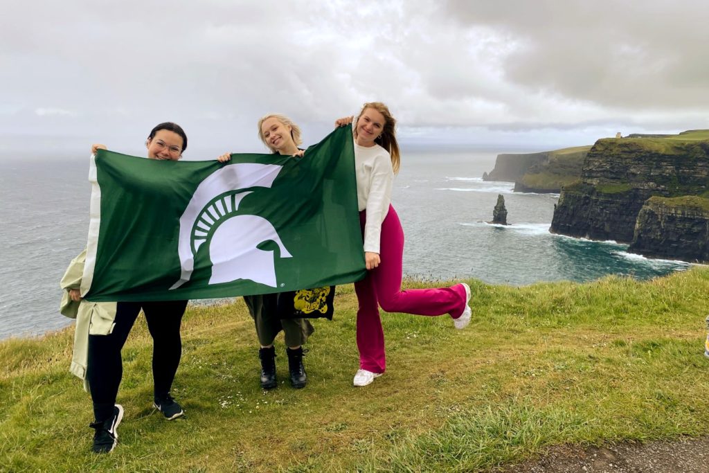 Three people on water horizon holding green flag with Spartan logo