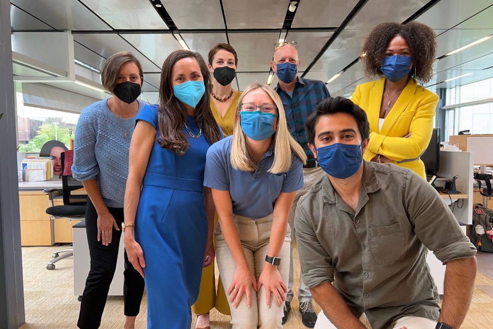 Seven people in masks pose for a group photo in an office.
