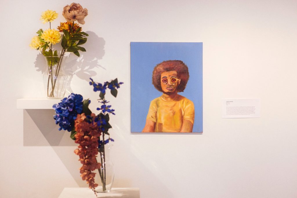 Photo of a painted portrait of a Black man next to flowers in vases.