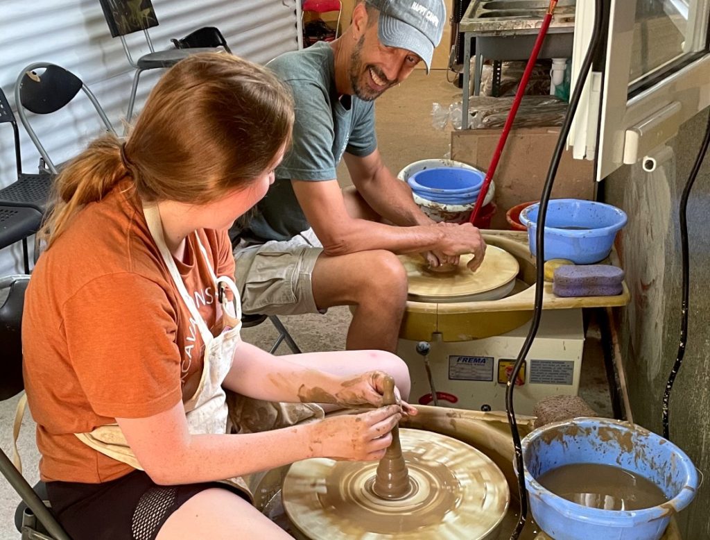 Two people sitting and looking at one another as they create pottery from clay with spinner.