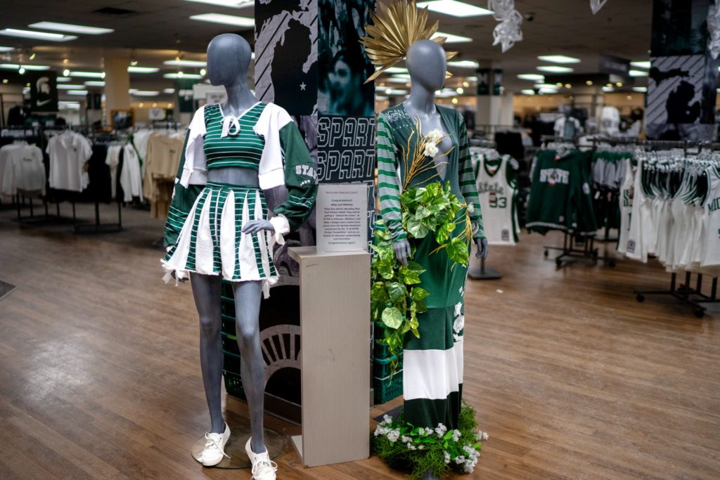 A picture of two distinct outfits in shades of green and white, in front of a background of clothing racks.