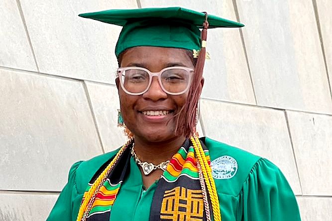 African American woman wearing glasses and an MSU green graduation cap and gown.