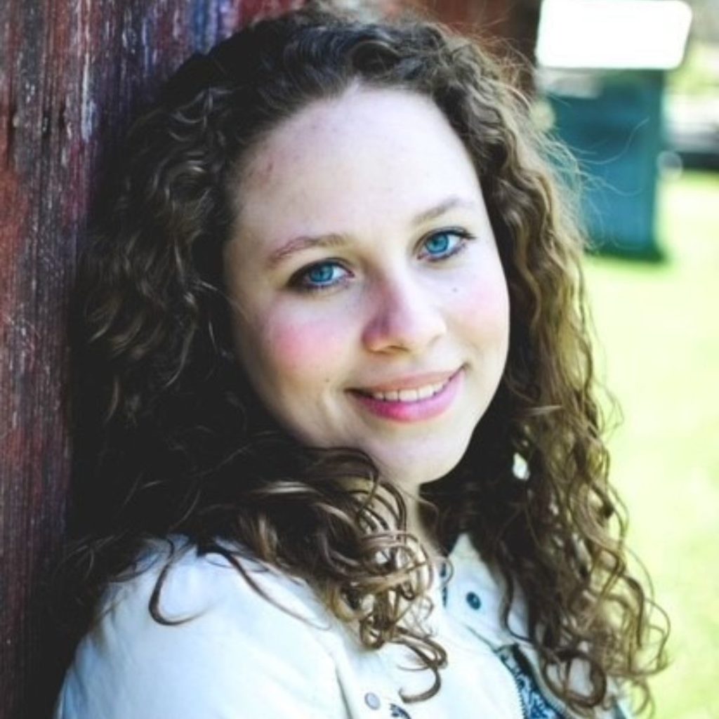 Portrait of a smiling woman with curly brown hair wearing a white jacket.