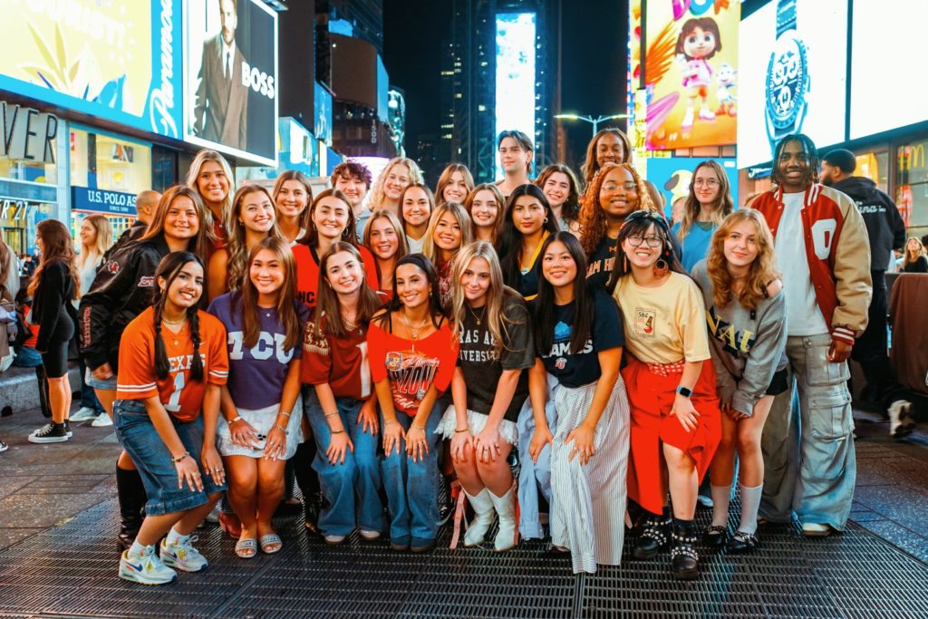 A picture of a crowd of students posing in front of a background of neon signs and advertisements.