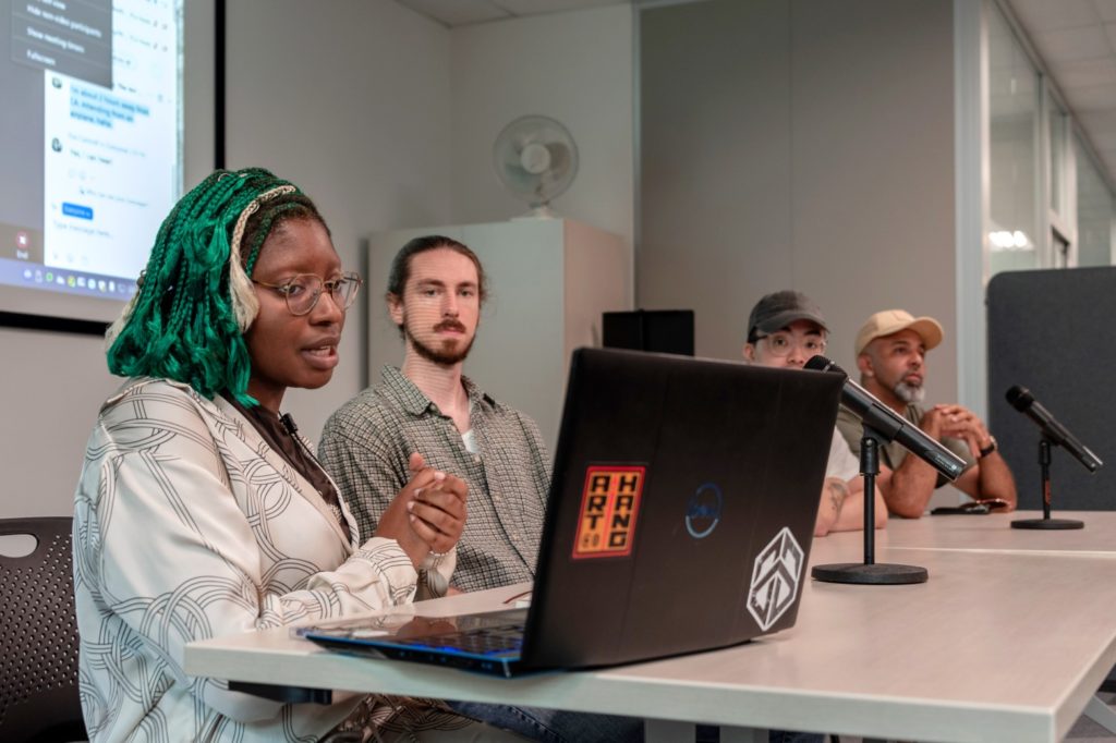 woman siting at a table with three men. She is sitting in front of a computer. 